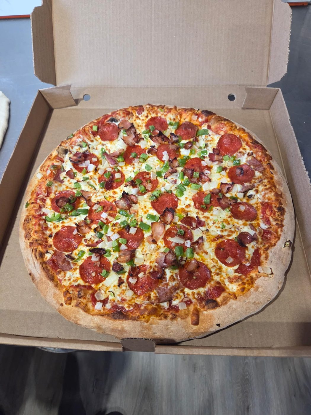 A fresh Old School pizza loaded with pepperoni, real bacon, green pepper and onion in a takeout box